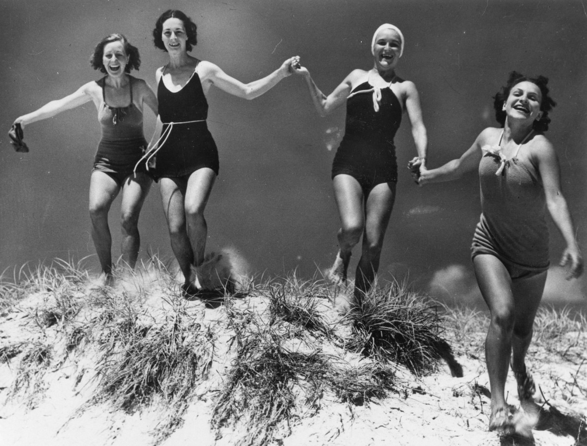 Four women running down a sand dune in swimwear