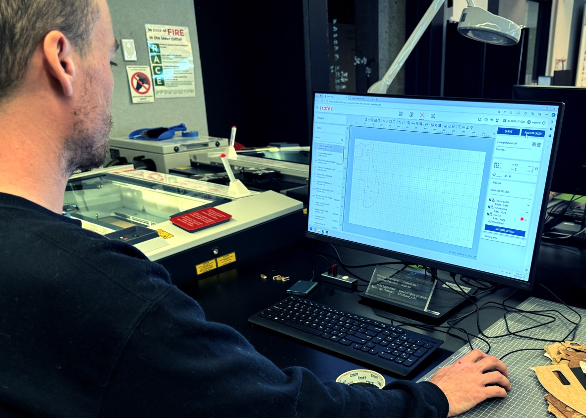 A photo of a person in front of a computer working on laser cutting software