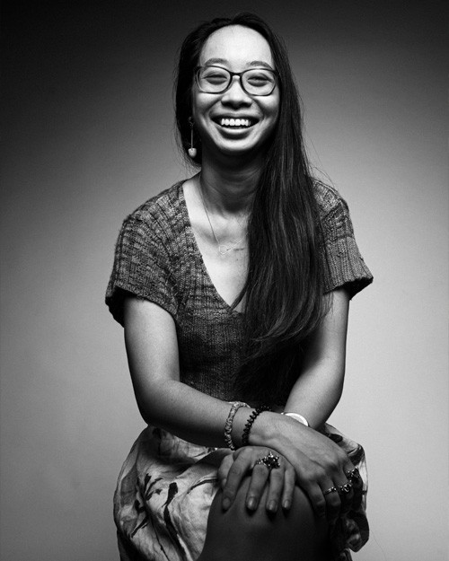 Yen-Rong Wong in a black and white photo She is seated with her hands folded smiling with glasses and her hair long