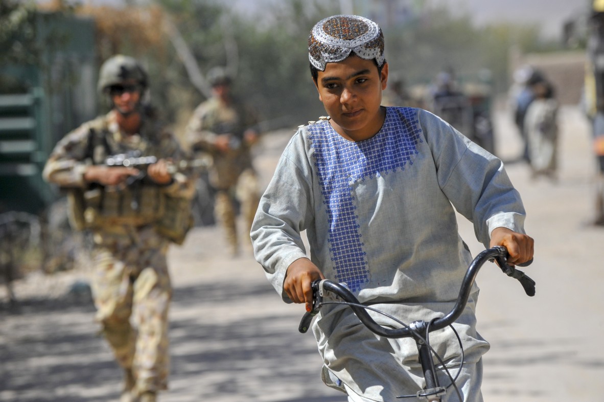 Young Afghan boy rides his bike past Townsville soldiers on foot patrol through the township of Tarin Kowt Afghanistan 2009