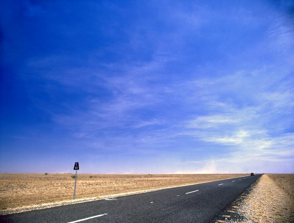 Long straight road on a empty plain with a blue sky above 