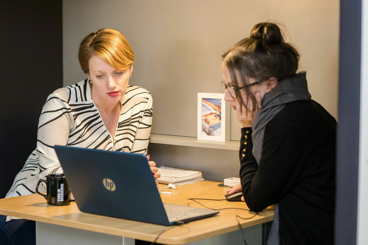 Two women sitting at a table looking at a laptop.