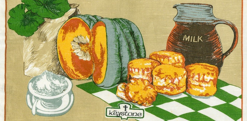 Tea towel printed with a still life of pumpkin scone ingredients on a green and white checkered tablecloth. 