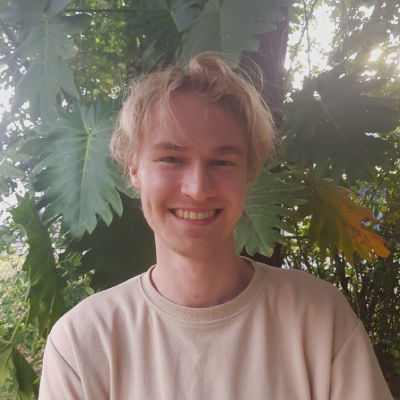 Headshot of Maxwell Freedman He is smiling at the camera standing in front of trees He has blonde hair and a pale brown shirt