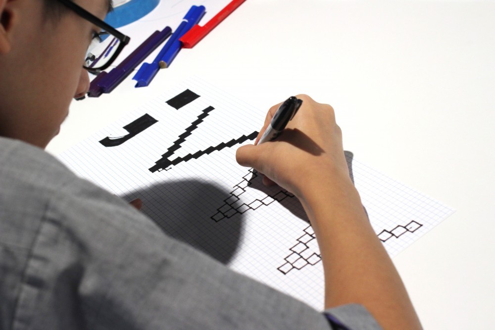 Student drawing letters on grid paper with pen