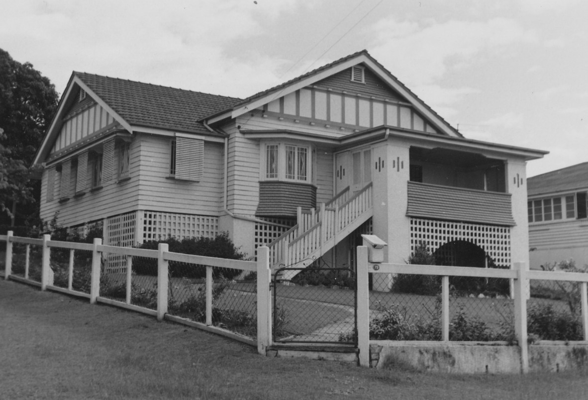 A multi gable house with a fence on a sloping lawn