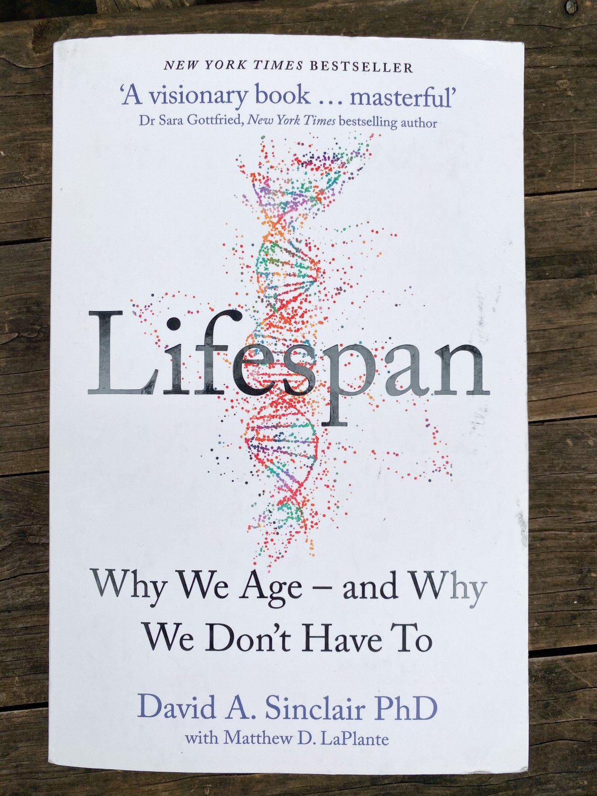 A close up of the book cover Lifespan by David A Sinclair which is white with a rainbow double helix in the centre