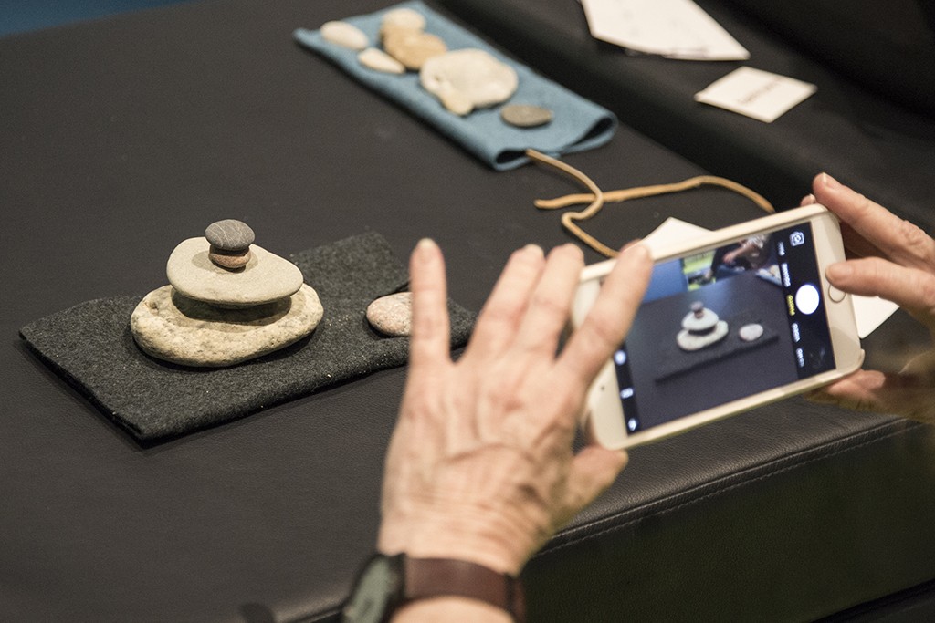 A woman takes an image of a stack of rocks on a table using an iPhone