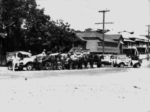 Bakery delivery trucks and horse carriages on a street. 