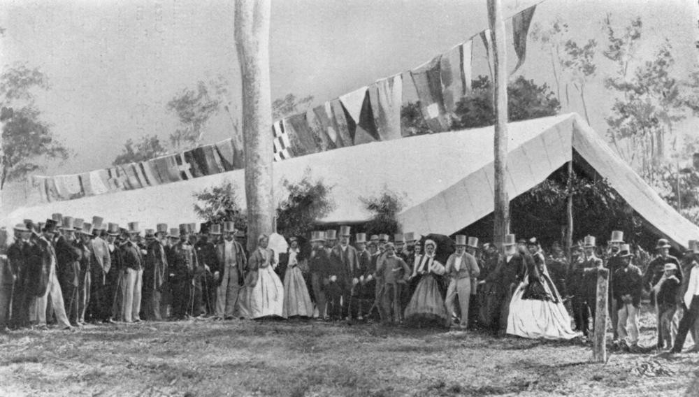 a group of people in fine dress and top hats stand outside a large tent 