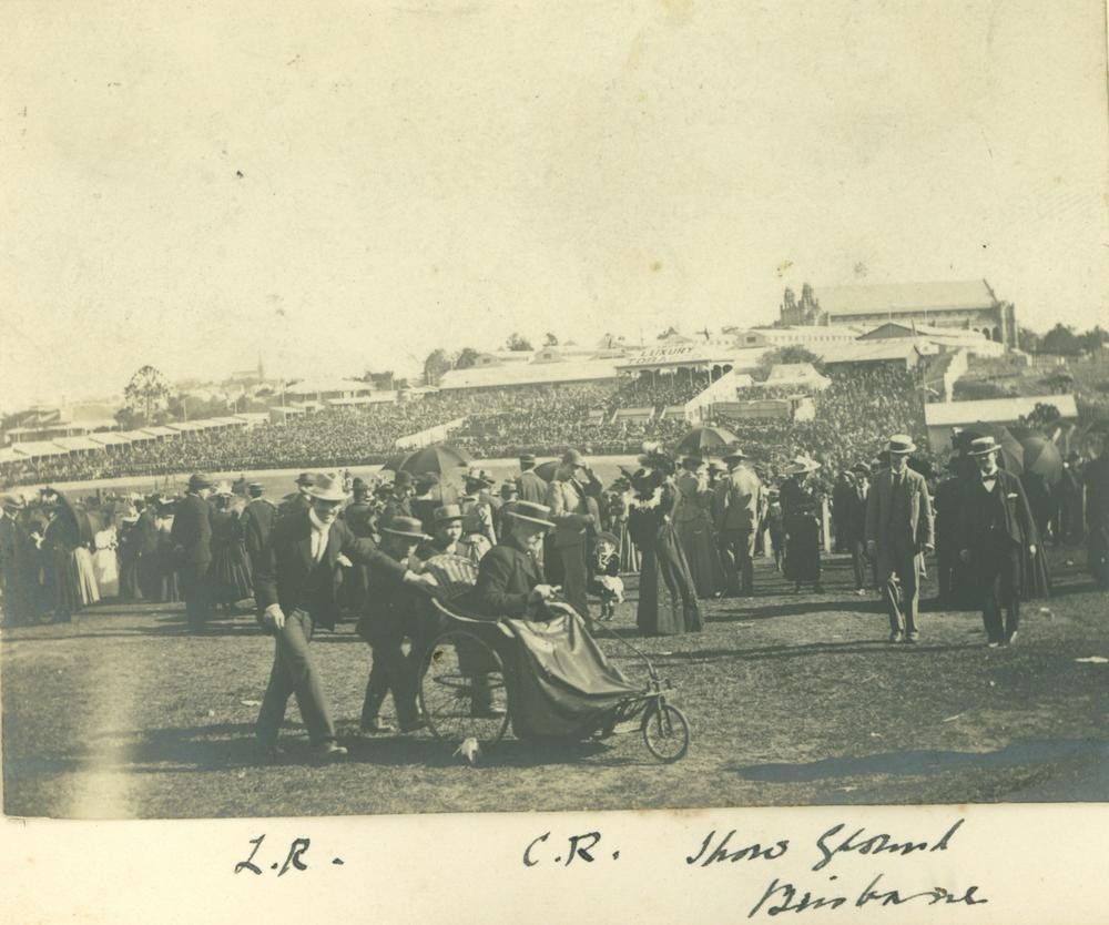 Lionel Rawson and two attendants pushing Chales Rawson's bath chair at the Brisbane Exhibition, ca.1912.