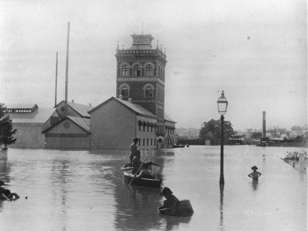view of a flooded brewery in west end with people in a boat in front 