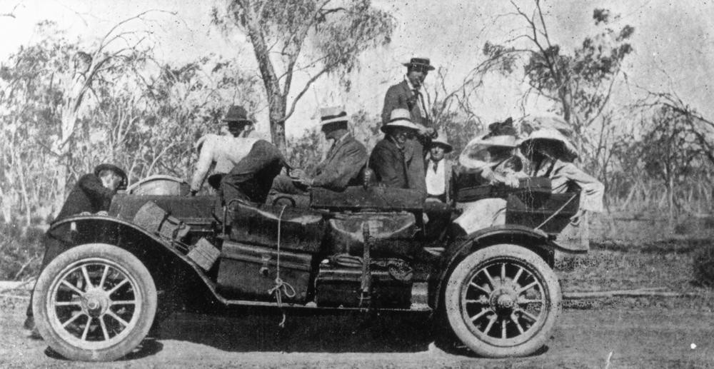 8 people sit in a large early american automobile