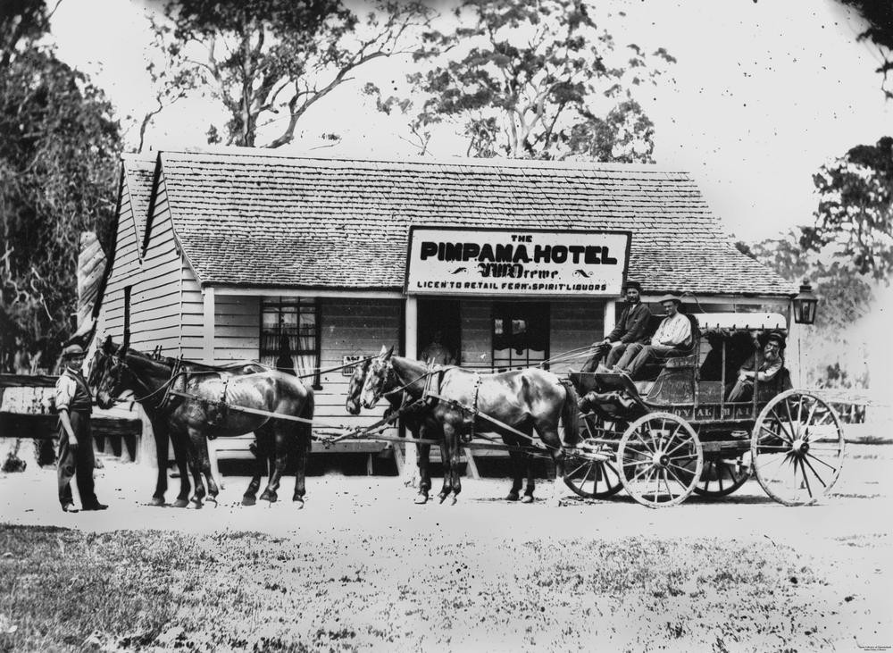 black and white image of people on a horse drawn cart outside a building with a sign saying Pimpama Hotel 