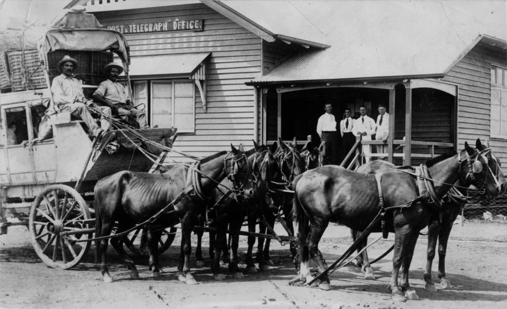 black and white image of two men on a horse and cart in front of a building 