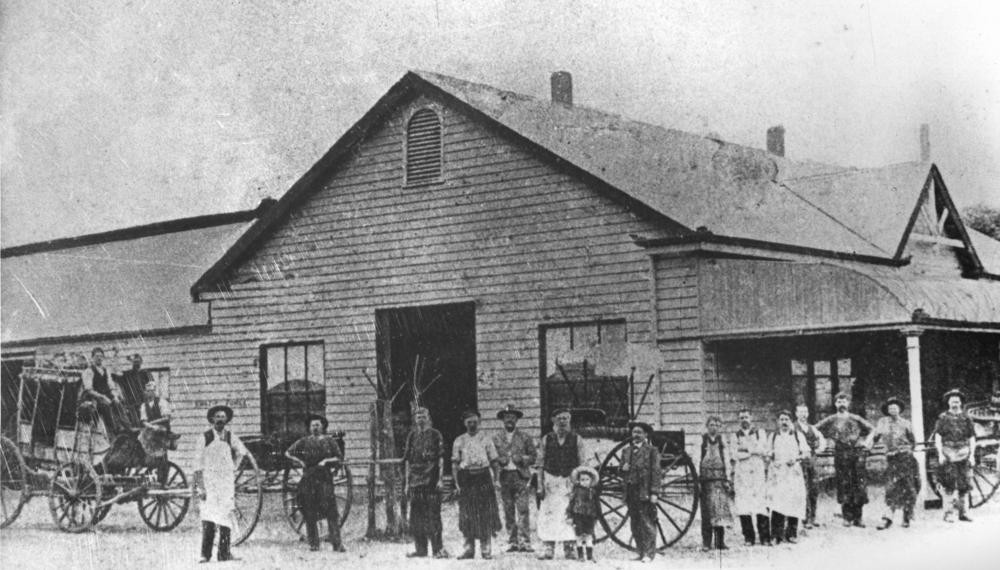 black and image of people standing outside a large wooden factory 