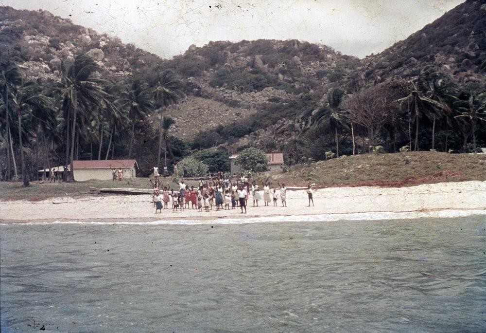 View of a beach on Dauan Island with a group of locals waving, Queensland 1968