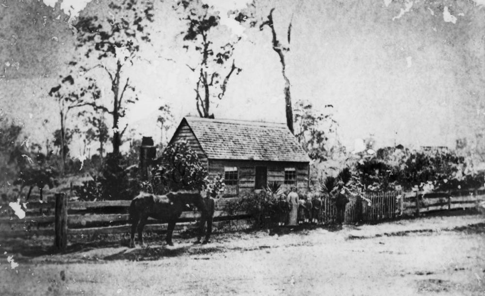 Black and white photo of a cottage with a family and horse outside.