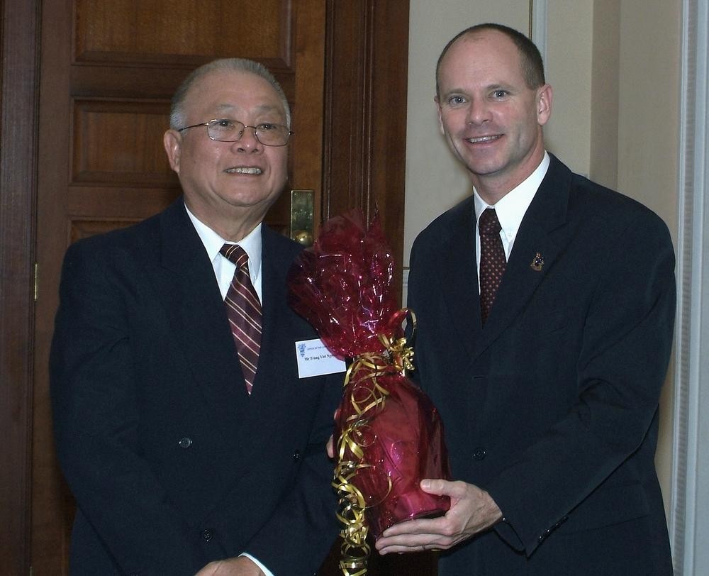 two men stand together with a wrapped present in between 