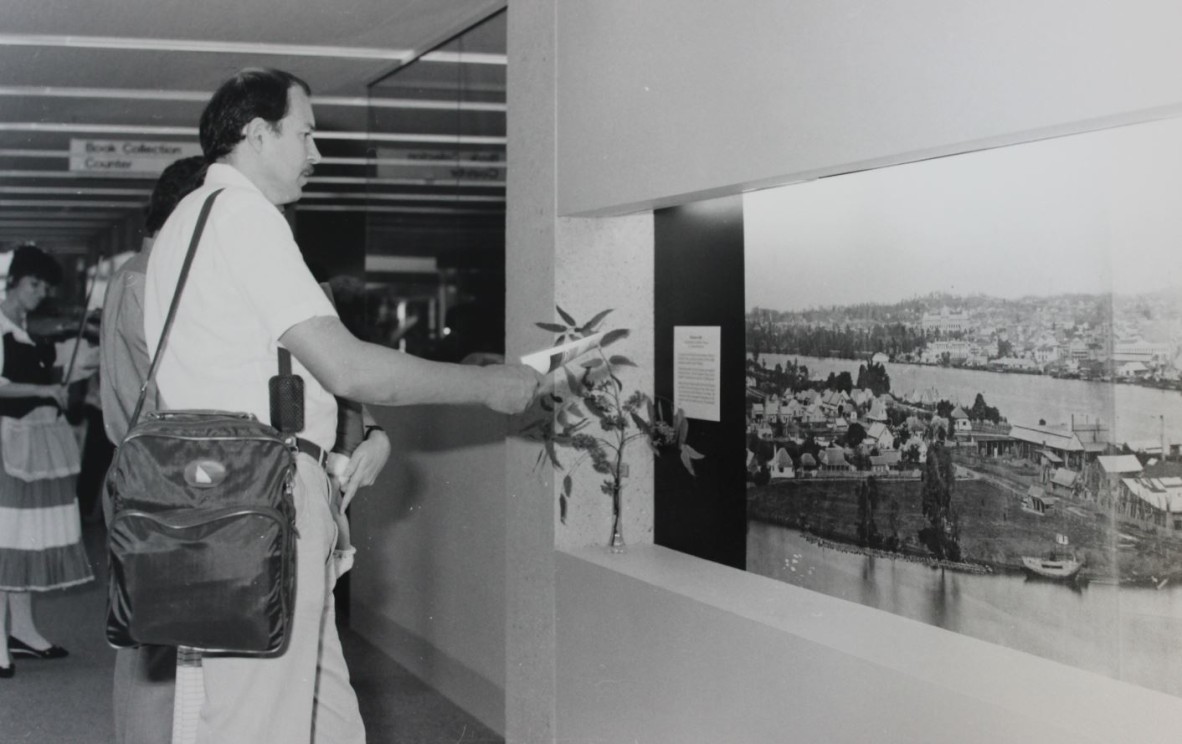 man with shoulder bag views image of river and houses in State library 