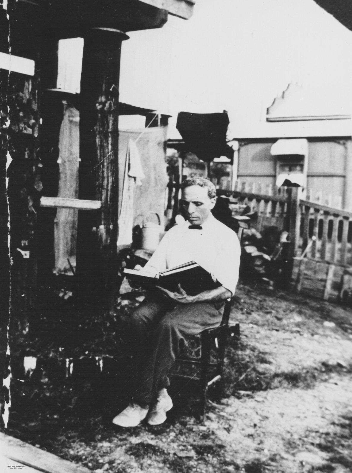 A man in a white shirt sits with a book in back yard behind a cafe
