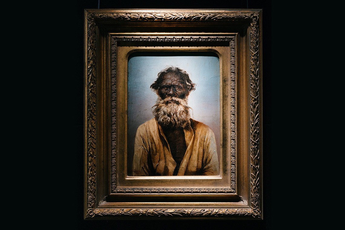 This oil painting by Swedish born artist Oscar Fristrom depicts Kirwallie or King Sandy a well-known Aboriginal elder of the Brisbane region  The painting is housed in an ornate gold coloured frame  it is a head an upper body depiction of an elderly Aboriginal man with a full grey white beard  He is wearing a white shirt which is open to his chest which shows signs of tribal scarification 