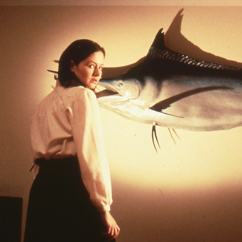 A still from Shirley Barretts film Love Serenade with a young woman standing in front of a taxidermied swordfish