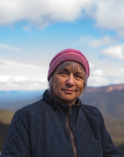 Maria van Neerven stands in a dark blue jacket and pink beanie at a mountain lookout