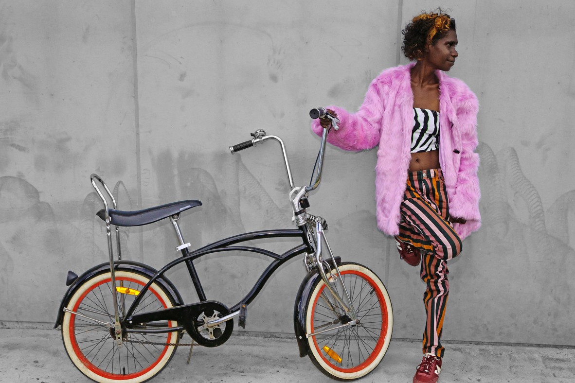 Ms. Daley leaning against a wall holding on to a flash black bike