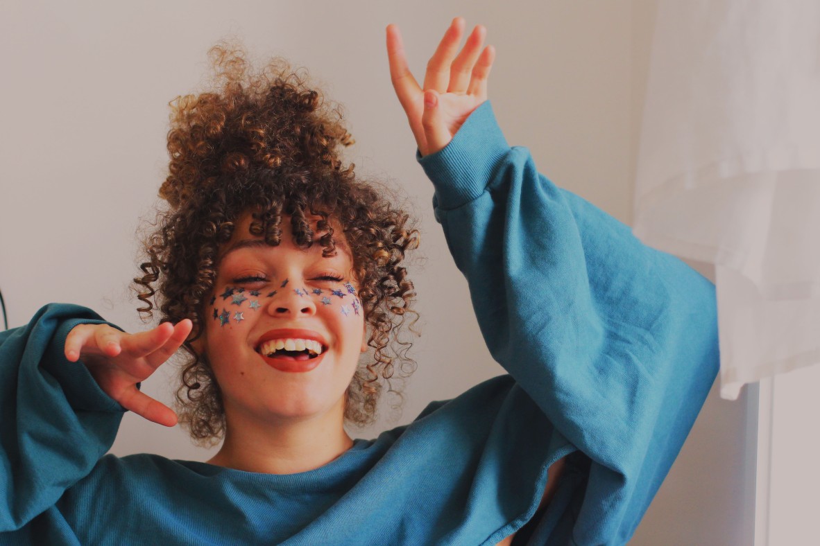 Self portrait of Tori-Jay, who has her eyes closed, smiling, wearing a big blue jumper