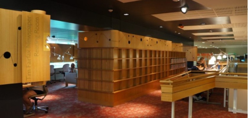library reading room with people sitting at desks and shelves with newspaper containers