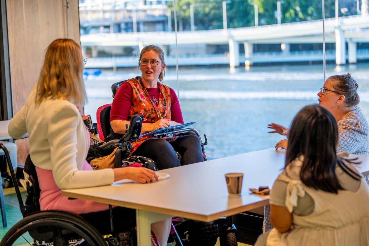 kathryn chats with attendees of the accessibility forum at The Edge, one attendee is also in a wheelchair. The Brisbane river is in the background