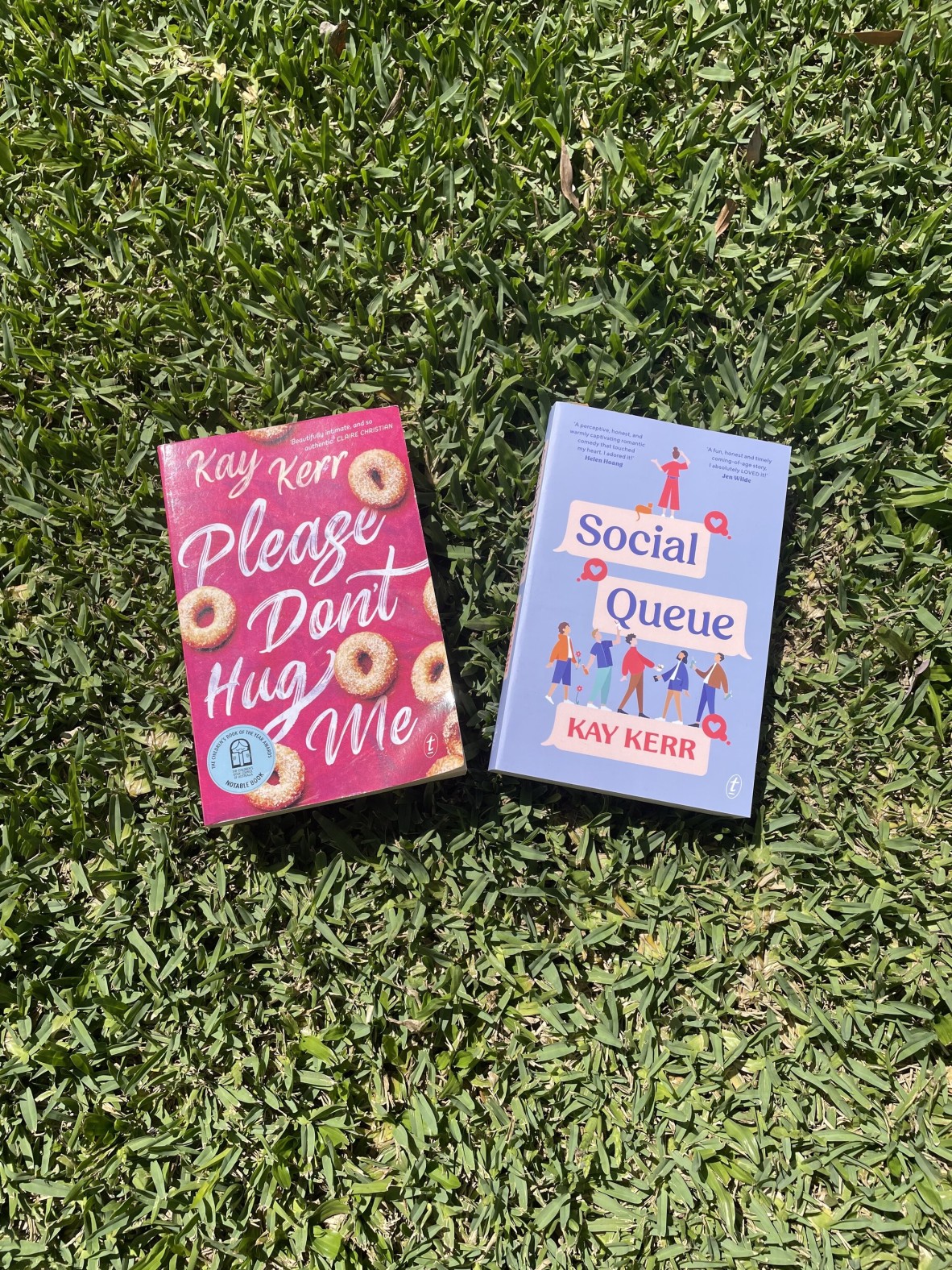 Kay's two books, Please Don't Hug Me and Social Queue, sit side by side on the grass