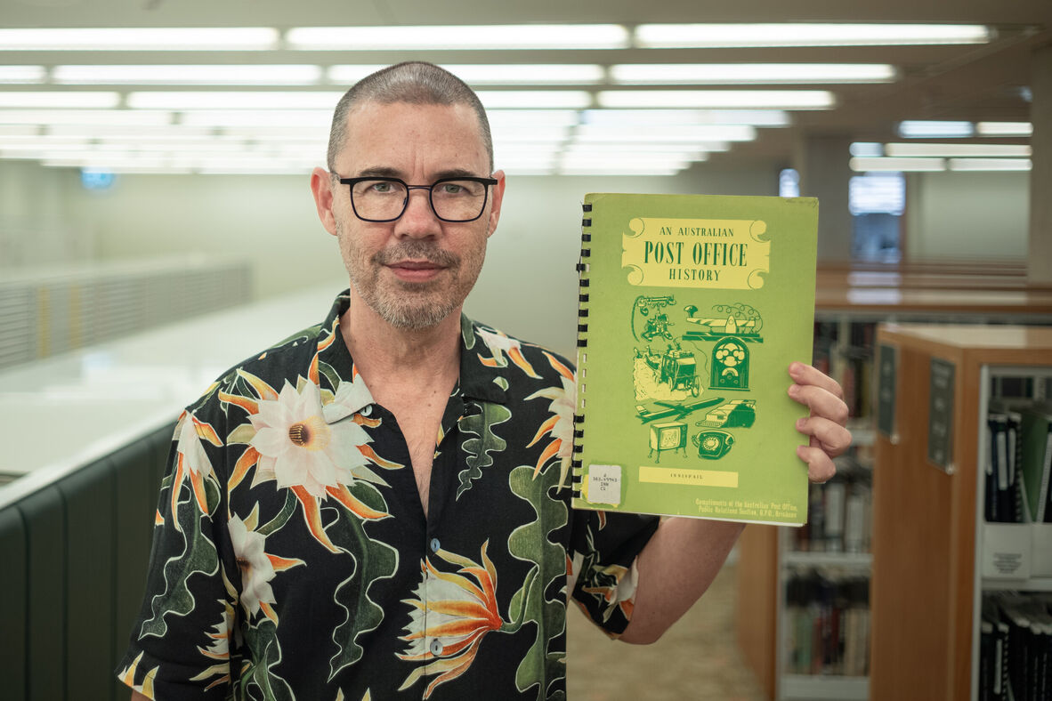 Steve MinOn stands in the John Oxley Library holding up a green pamphlet