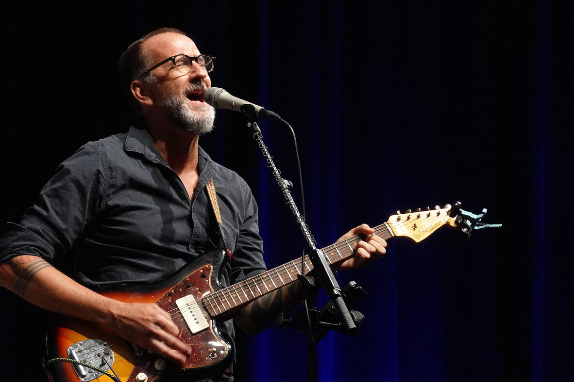A musician is singing at a microphone and playing a guitar