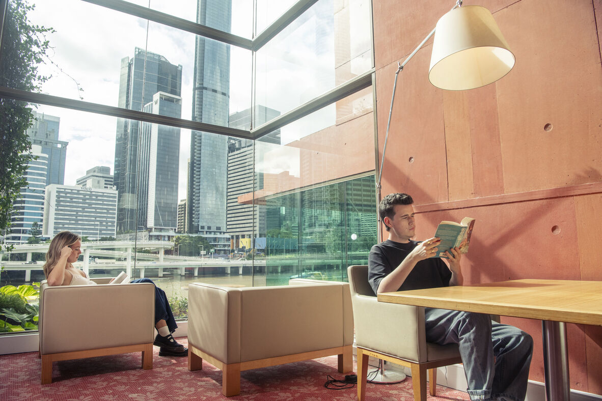 Two young people read books in the library, the city in the background