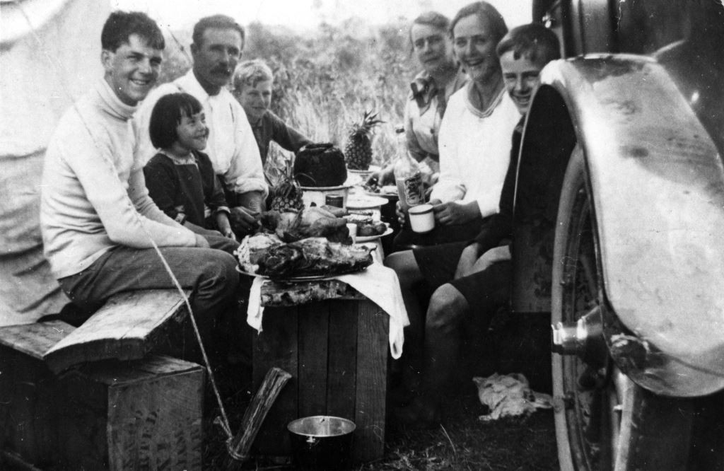 Family group of two adults and 5 children eating lunch beside a truck, 1918
