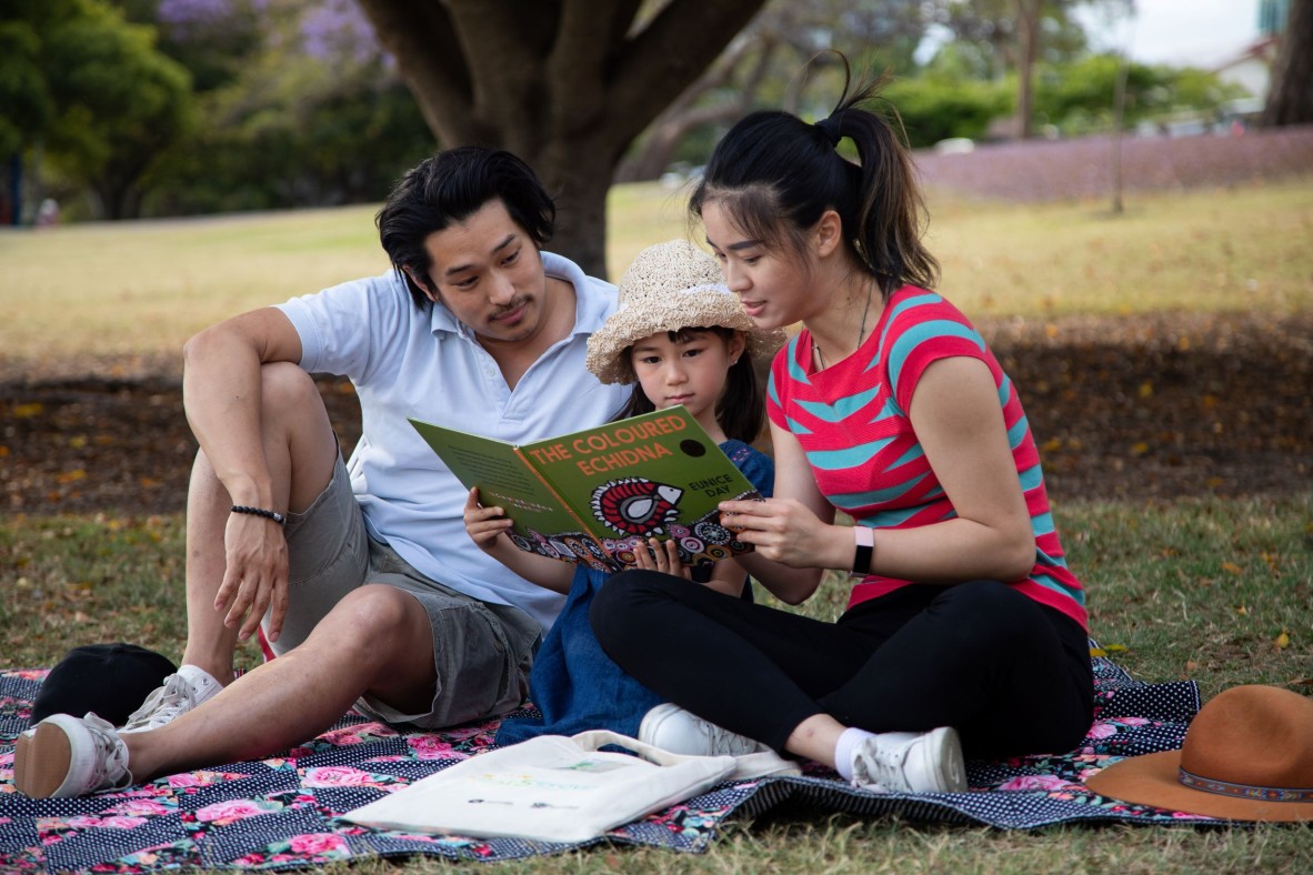 Family in a park reading a picture book called The Coloured Echidna