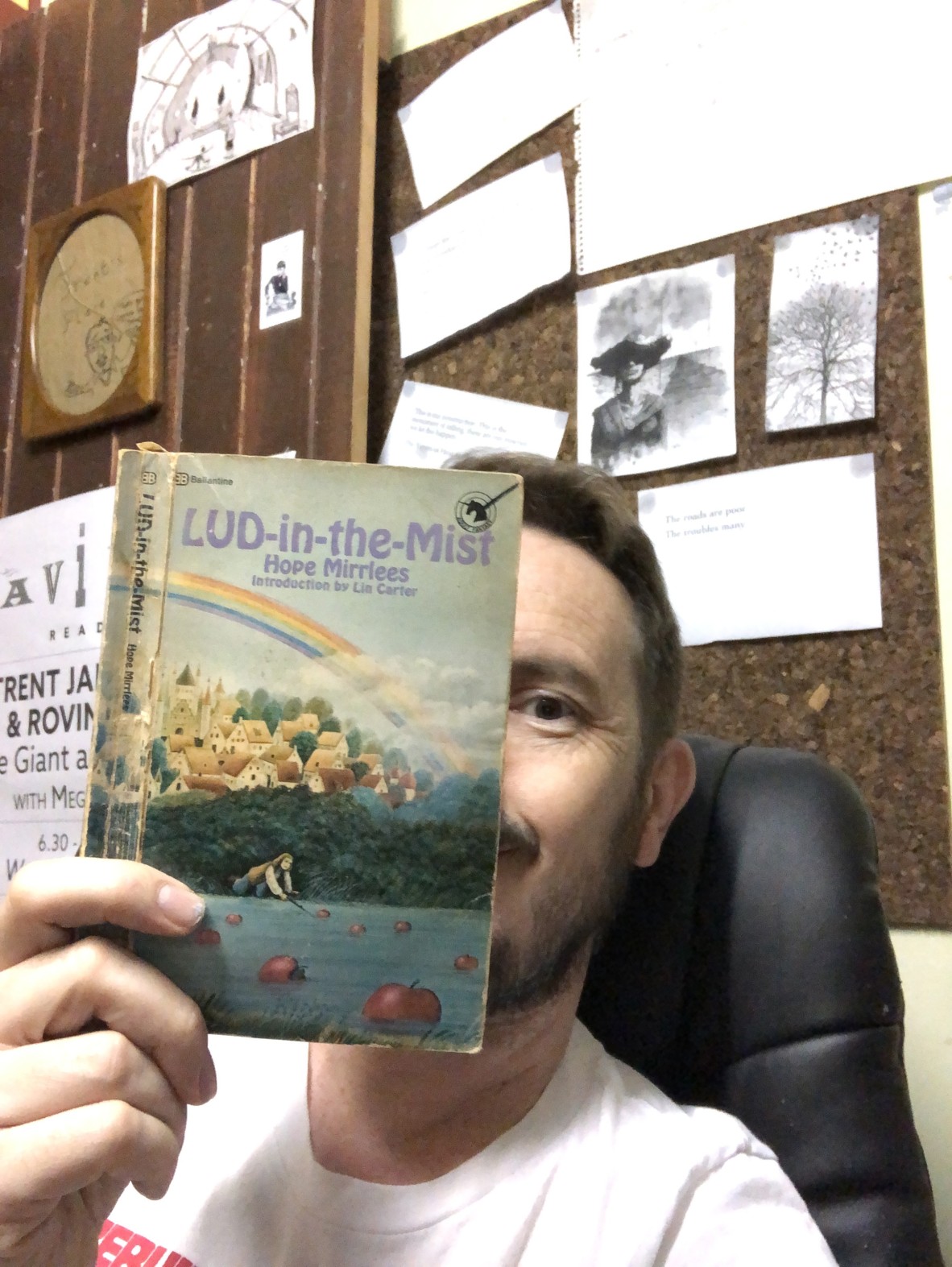 Trent Jamieson holds up a copy of Lud-in-the-mist by Hope Mirrlees Trent sits in front of a pin board